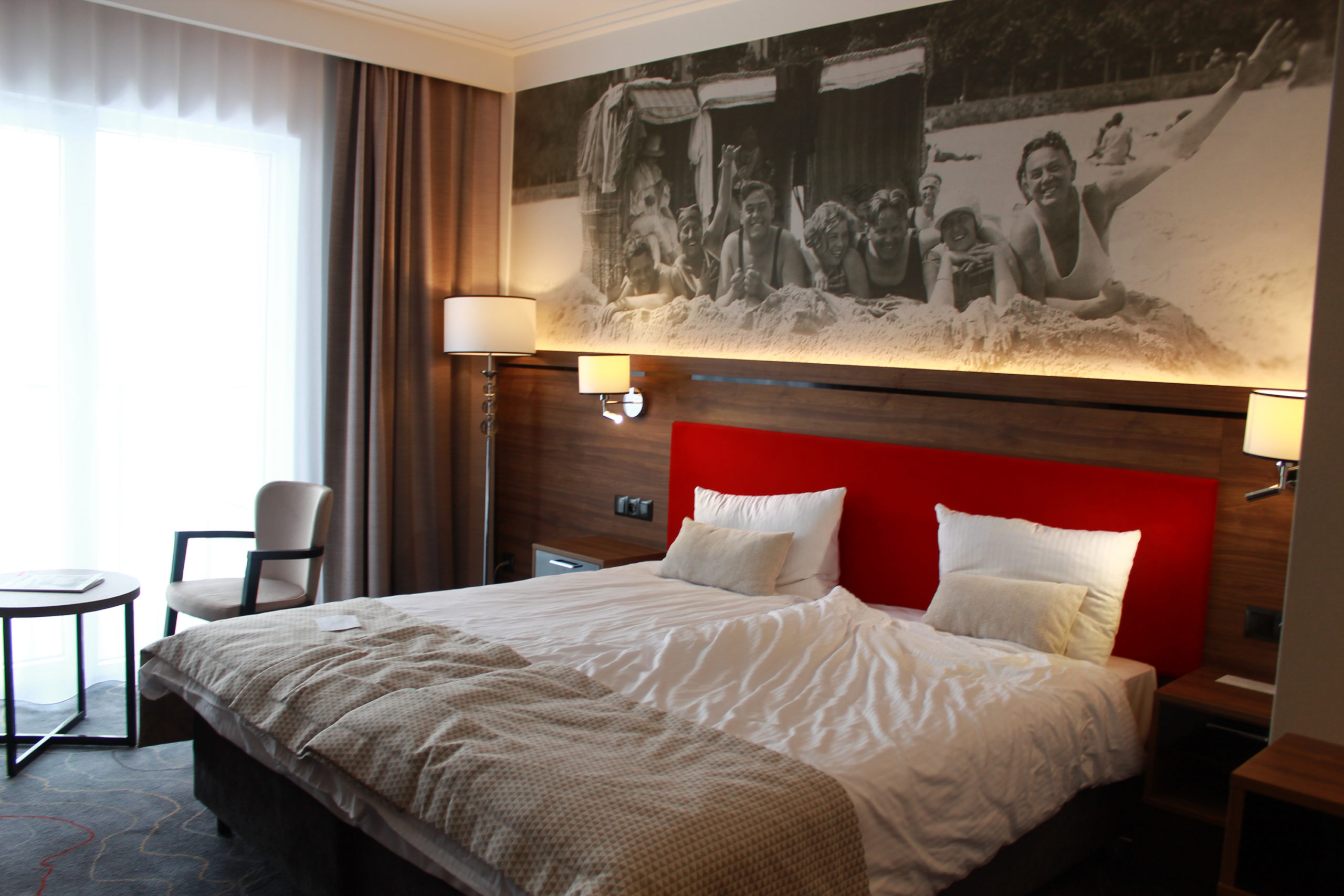podwójne łóżko w hotelu, nad łóżkiem biało-czaje zdjęcie ludzi na plaży