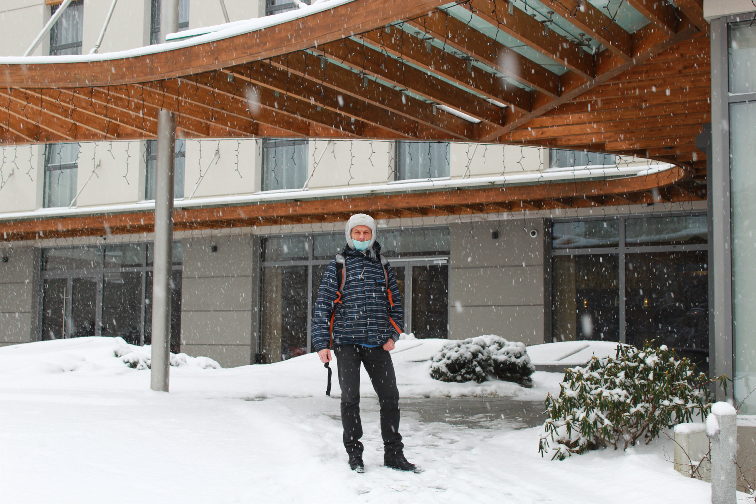mężczyzna w zimowym ubraniu przed wejściem do hotelu, pada śnieg